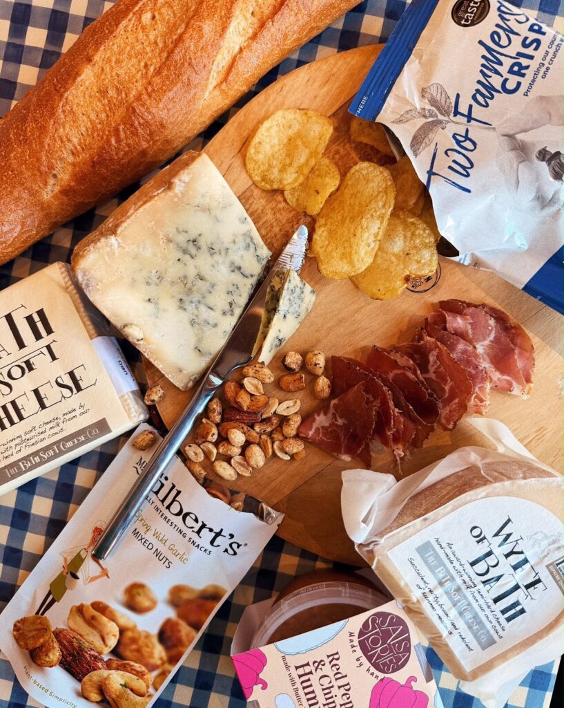 Blue cheese, cured ham, crisps and nuts on a board with a baguette