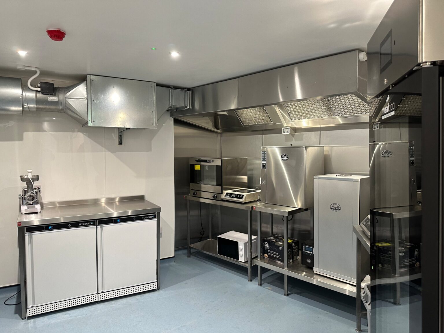 The stainless-steel kitchen under the Root & Ember shop, with smoker cabinets, oven and extraction hood